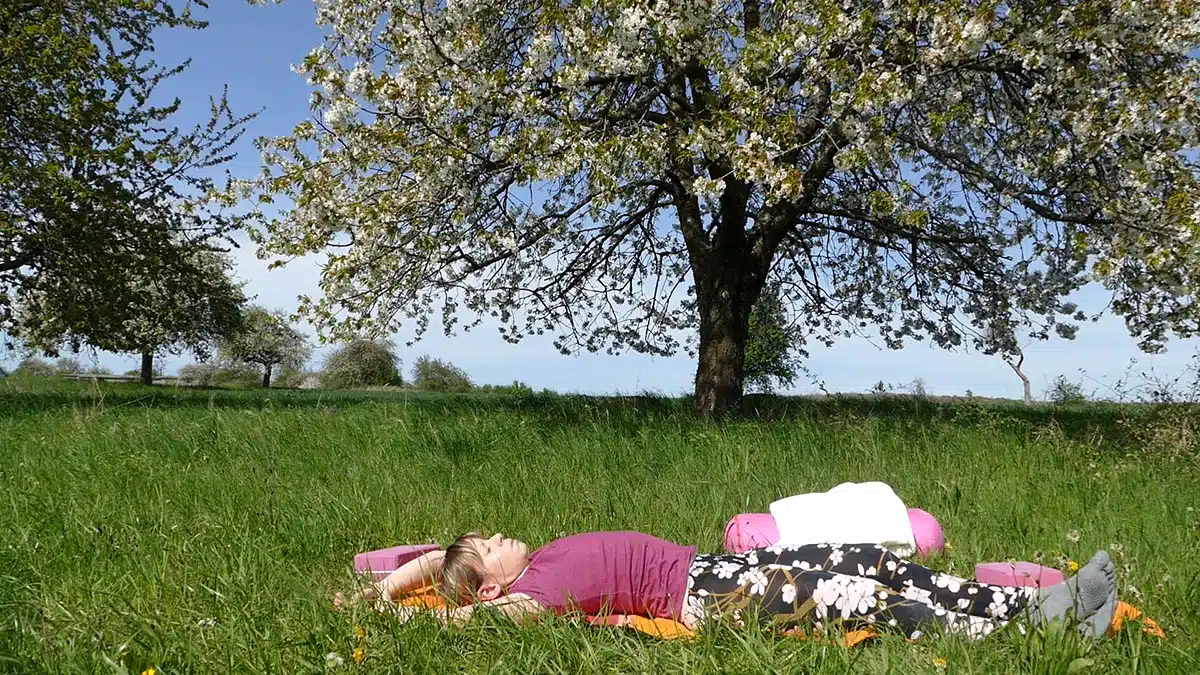 Frau liegt entspannt auf Yoga-Matte unter blühendem Kirschbaum