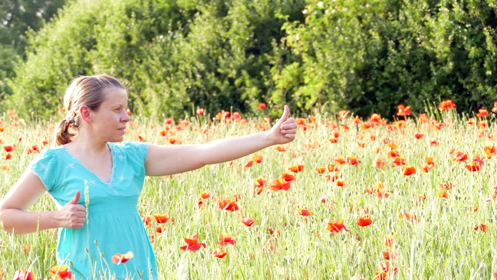 Frau in türkisem Kleid macht Qigong-Bewegung in Mohnblumenfeld