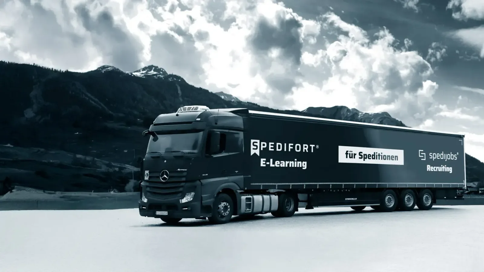 Mercedes-Lkw mit SPEDIFORT E-Learning-Beschriftung in alpiner Berglandschaft