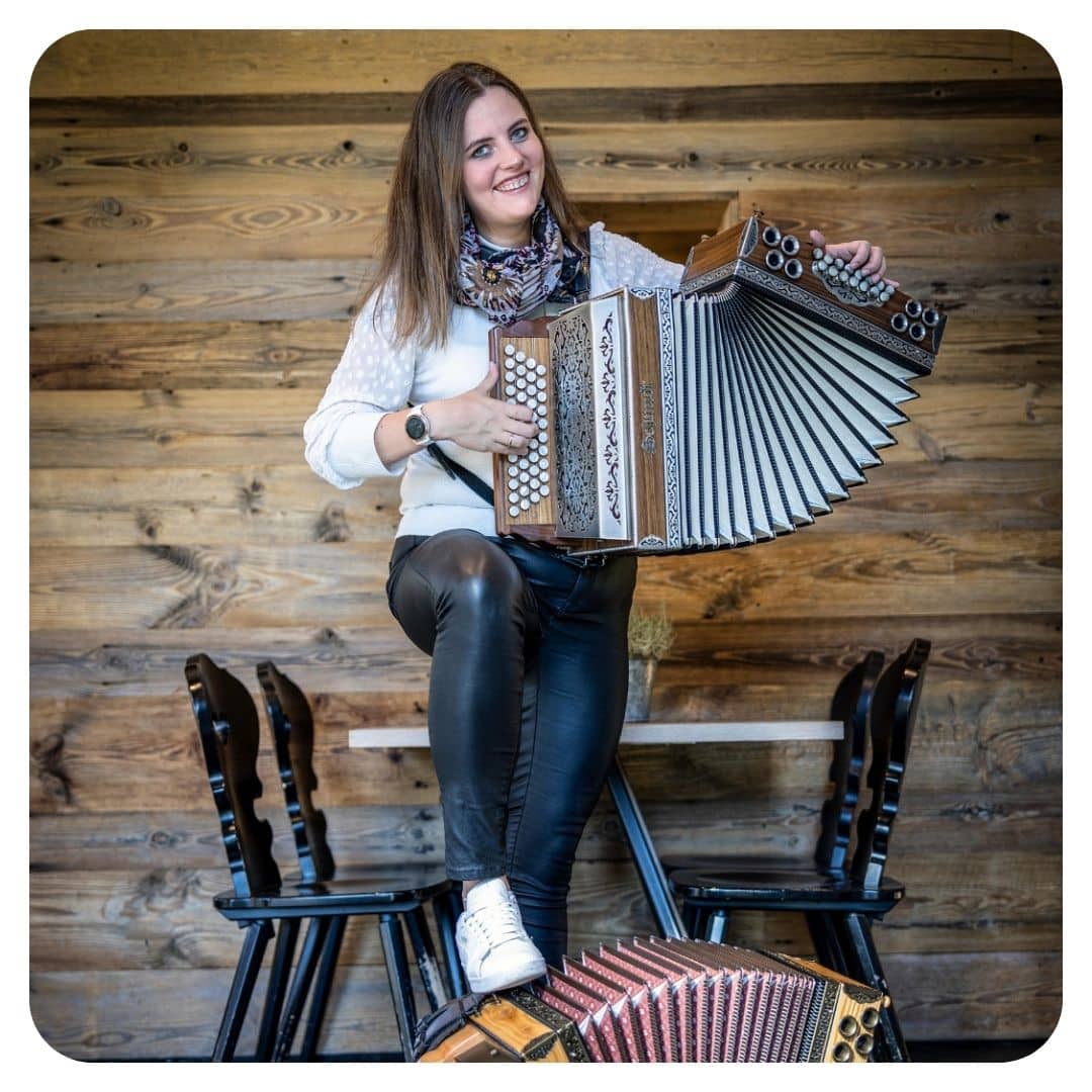 Junge Frau mit Steirischer Harmonika vor Holzwand sitzend