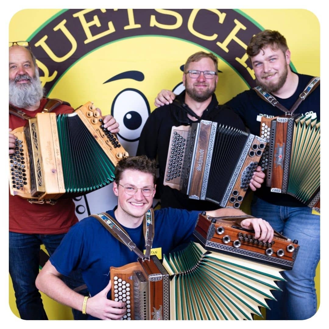 Vier Männer mit Steirischen Harmonikas vor gelbem Quetschn-Logo