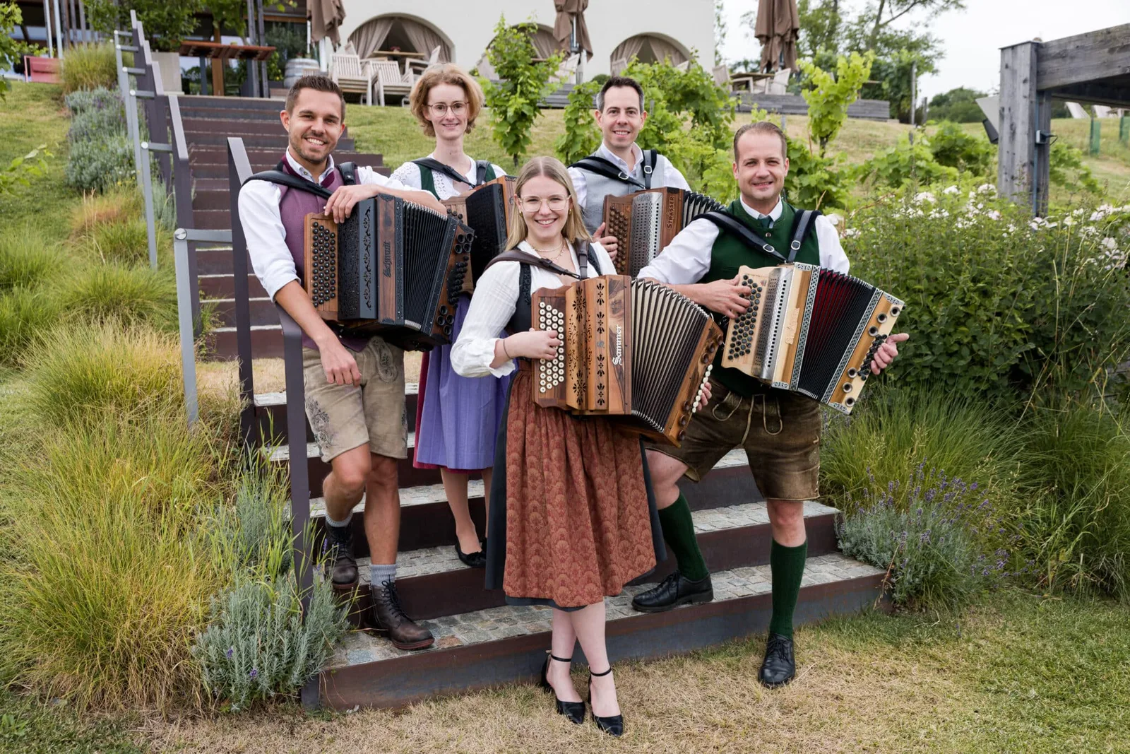 Fünf Quetschn Academy Lehrer in traditioneller bayerischer Tracht mit Harmonika auf Treppe