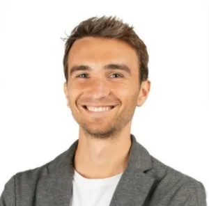 Porträt eines jungen Mannes mit braunen Haaren, grauem Blazer auf weißem Hintergrund