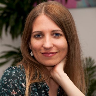 Porträt Aline Brandstetter, Frau mit braunen Haaren und Lächeln vor grünem Hintergrund