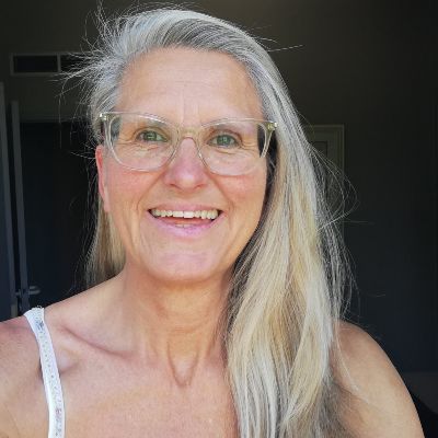 Porträt Ilka Henriette Weiß, ältere Frau mit grauem Haar und Brille vor dunklem Hintergrund