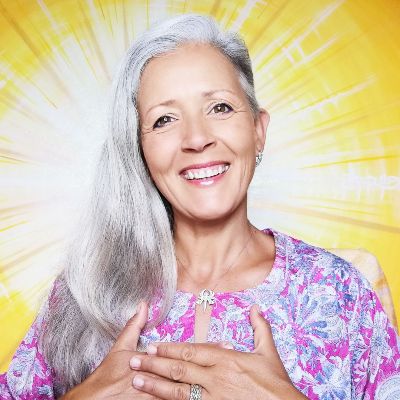 Porträt einer älteren Frau mit grauem langem Haar und lila-rosa Blumenshirt auf gelbem Strahlenhintergrund