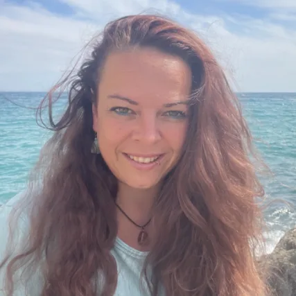Porträt einer jungen Frau mit rötlich-braunem langem Haar am Strand vor Meer und Himmel