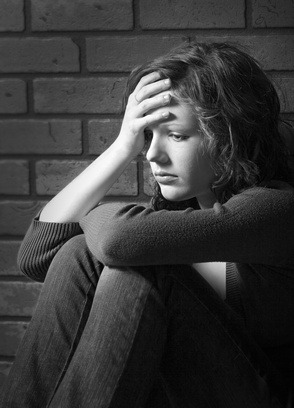 Schwarzweiß-Porträt einer traurigen Frau mit Hand an der Stirn vor Backsteinwand