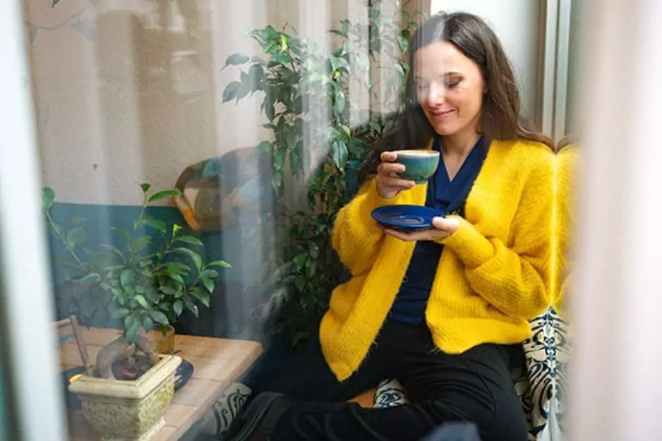 Frau in gelbem Cardigan trinkt Tee neben Pflanze, Nervensystemregulation