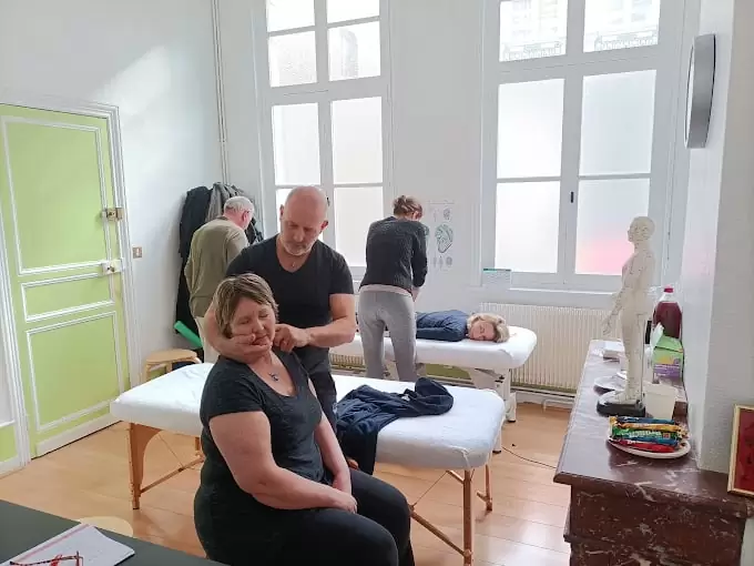 Schulungsraum mit Therapeut und mehreren Patienten auf Massagebänken, grüne Tür