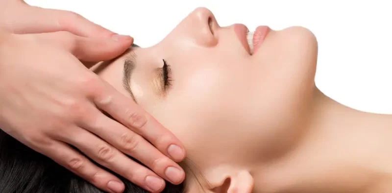Hände eines Therapeuten führen Gesichtsmassage durch bei entspannter Frau