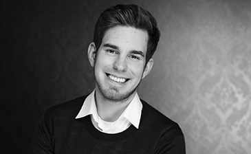Porträtfoto von Hendrik Klöters, junger lächelnder Mann in schwarzem Shirt mit weißem Kragen