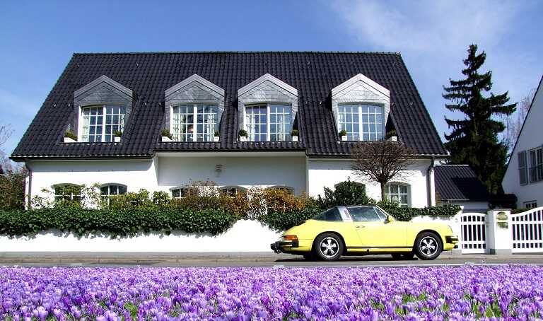 Luxusvilla mit weißer Fassade, schwarzem Dach und gelbem Sportwagen in Blütenfeld