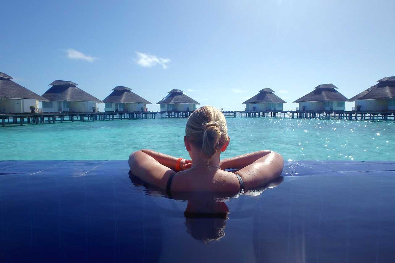 Frau entspannt in Infinity-Pool mit Blick auf tropische Luxus-Bungalows im Meer