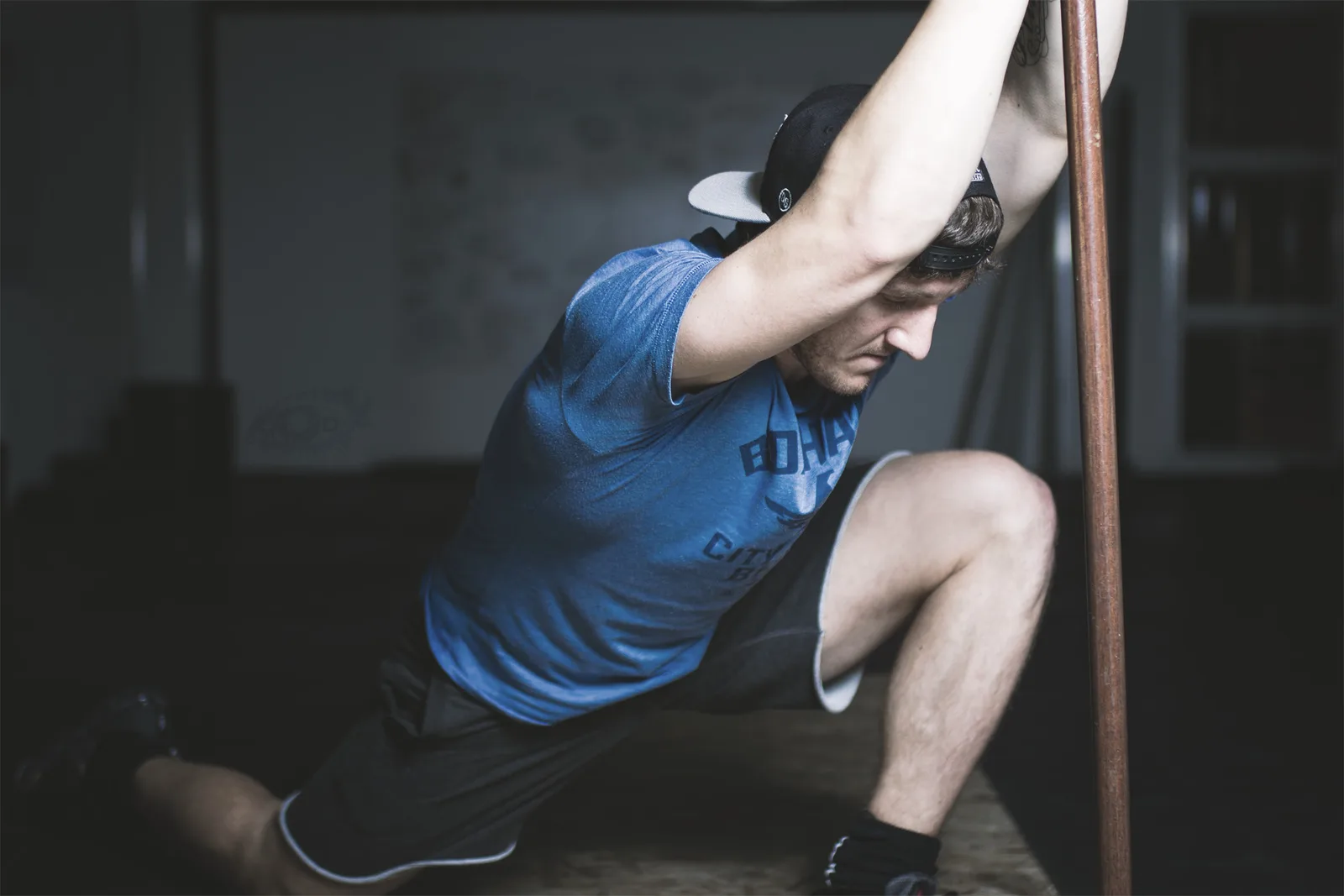 Mann in blauem Shirt führt Schulterübung an Stange im Fitnessstudio durch