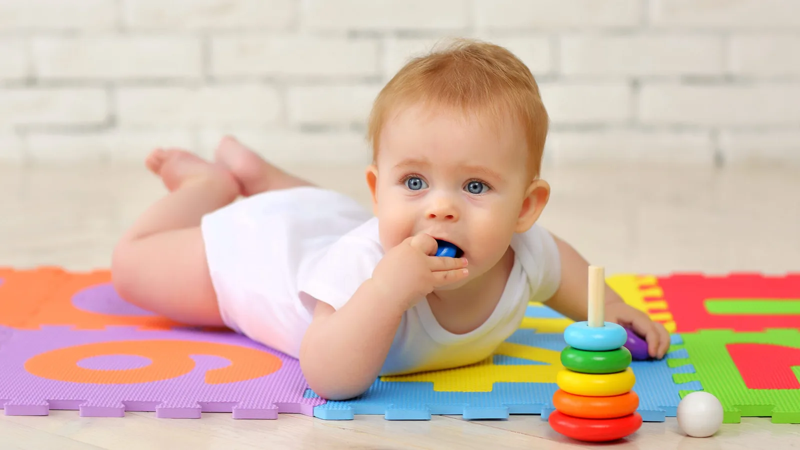 Kleines Baby auf buntem Spielmatte mit Rasseln und Spielzeug, exploriert Umgebung