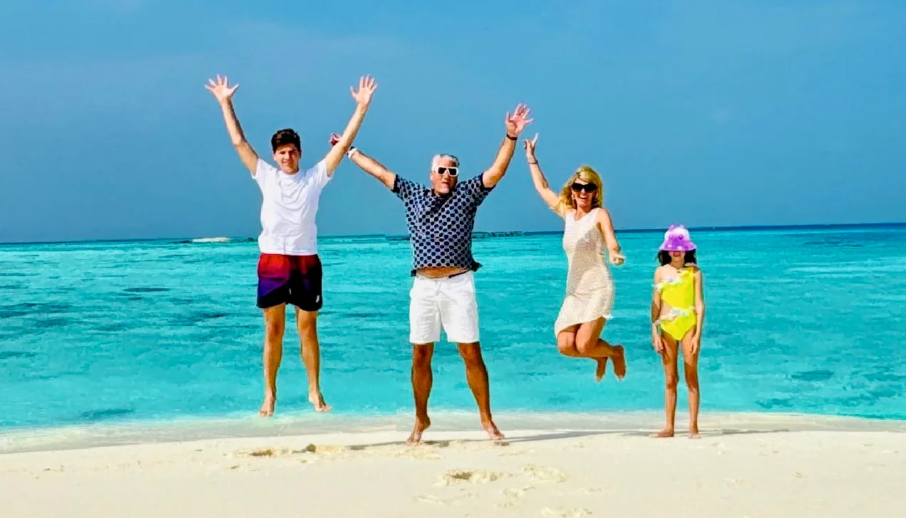 Familie mit vier Personen springt vor blauem Meer und Strand in die Luft