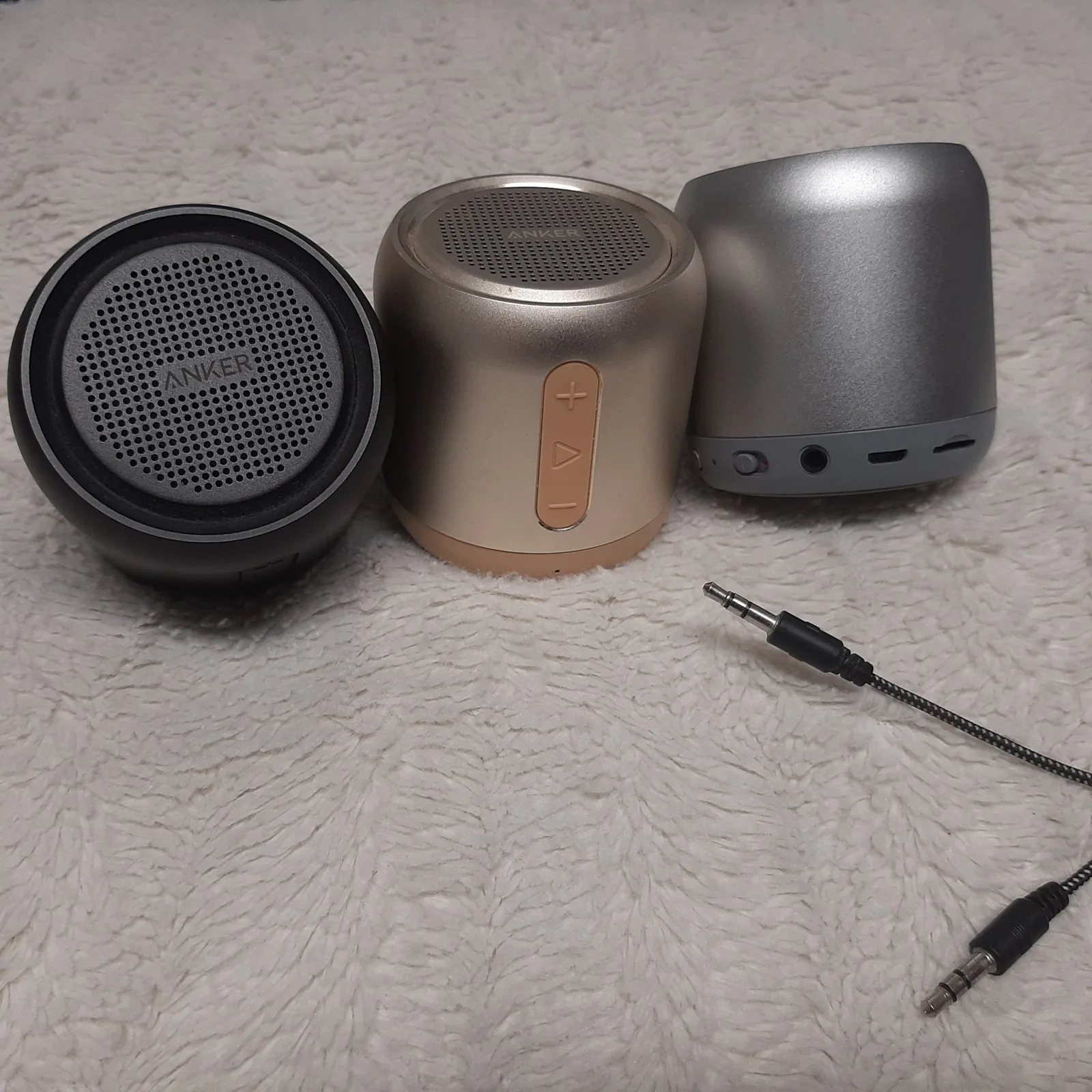 Produktabbildung von drei Anker Soundcore Mini Bluetooth-Lautsprechern in verschiedenen Farben mit Audiokabel