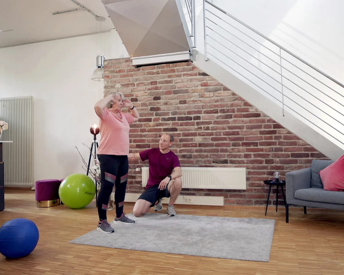 Trainerin und Trainer beim Hanteltraining in hellem Fitnessstudio mit Ziegelwand