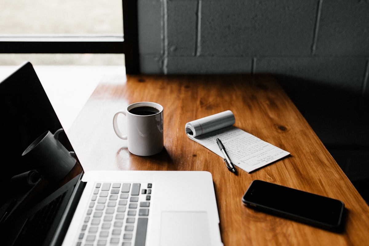 Arbeitsplatz mit Laptop Notizbuch und Kaffee symbolisiert Rauchfrei-Plan