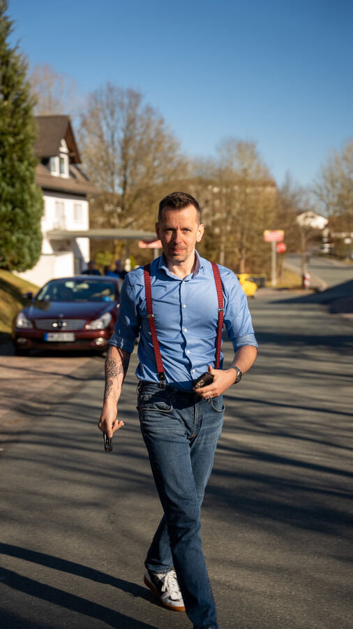 Patrick Helm joggt in blauem Hemd mit roten Hosenträgern durch Wohnstraße