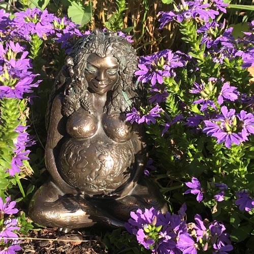 Bronzeskulptur schwangerer Frau vor lila Blüten, Schoßraum-Erkenntnisse