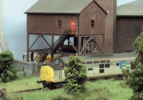 Modellbahnanlage mit Wasserturm, gelbem Güterwagen und grüner Vegetation