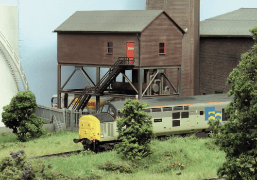 Diorama einer Modellbahnanlage mit Wasserturm, gelbem Güterwagen und realistischer Landschaftsgestaltung