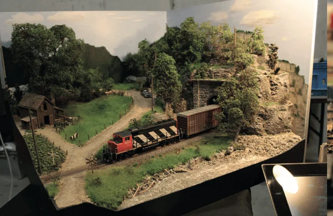 Großformat-Modellbahnanlage mit rotem Güterzug, Häusern, Vegetation und Felsszenerie