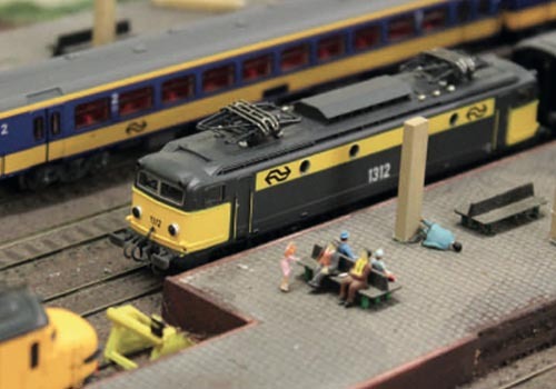 Detailaufnahme einer Modellbahnanlage mit schwarzgelber Lokomotive und Personen