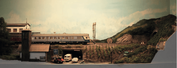 Modellbahnanlage mit Lokomotive, Personen- und Güterwagen, Bahnhof und Berglandschaft