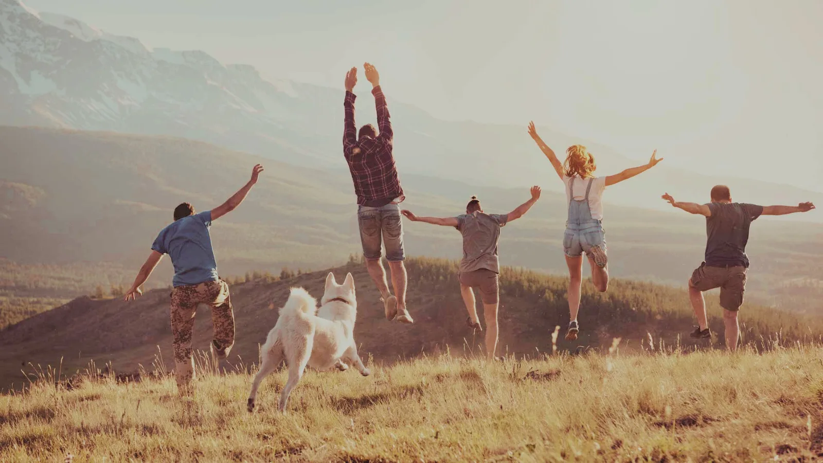 Familie mit Hund springt in Berglandschaft
