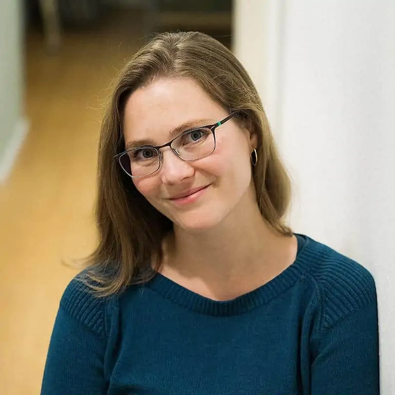 Porträt einer Frau mit Brille und braunen Haaren vor unscharfem Hintergrund