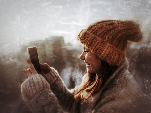 Frau mit oranger Mütze hält Smartphone in schneeiger Landschaft