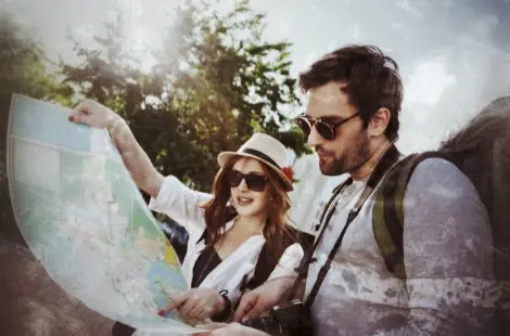 Zwei Touristen mit Sonnenbrille und Hut studieren eine Landkarte während einer Stadttour