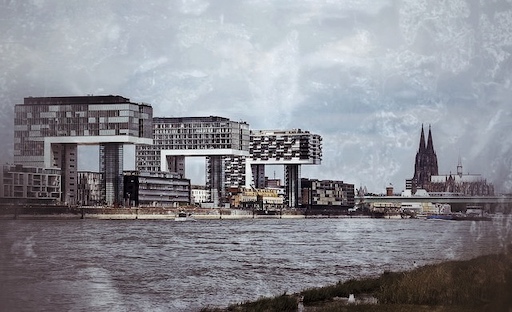 Kölner Rheinufer mit modernen Gebäuden, Dom und Kirchtürmen im Hintergrund, bewölkter Himmel