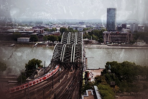 Luftaufnahme Hohenzollernbrücke Köln mit roten Zügen, Rhein, Skyline und bewölktem Himmel