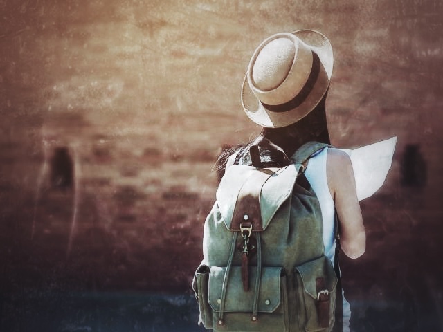 Person mit Rucksack, Strohhut und Landkarte von hinten vor unscharfer alter Hausfassade