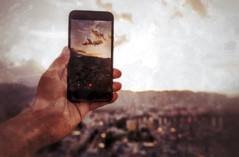 Hand hält Smartphone mit fotografiertem Himmel über Stadtlandschaft