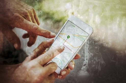 Hände halten Smartphone mit Kartendarstellung und grünem Navigationspunkt