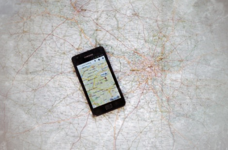 Smartphone mit Navigationskarte auf Papierkarte mit handgezeichneten Routen