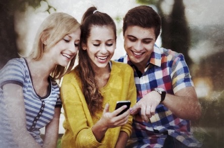 Drei lachende Freunde schauen auf Smartphone während gemeinsamer Stadtrallye