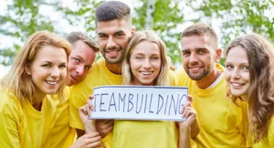 Sechs Personen in gelben Shirts halten Teambuilding-Schild in Gruppe
