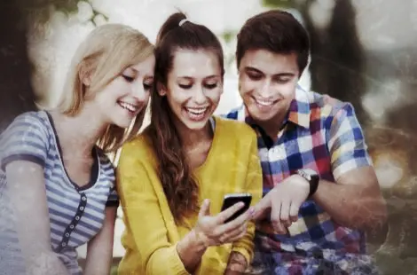 Drei junge Menschen mit Smartphone, lächelnd und konzentriert auf das Gerät