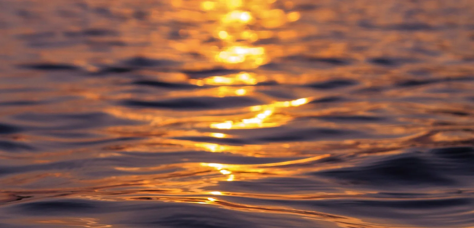 Sonnenuntergang über Wasser mit goldenen Spiegelungen, abstrakte entspannende Naturaufnahme