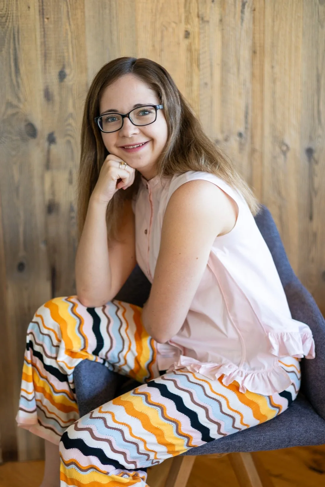 Selflove Vibes – Onlinekurs für mehr Selbstwert von Marie Kremer 11 Marie Kremer Porträt sitzend mit Brille und gemusterter Hose vor Holz-Hintergrund