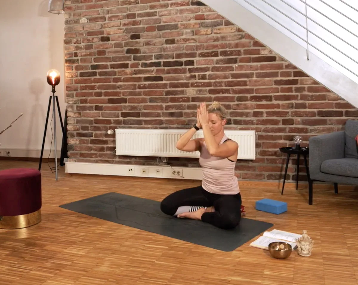 Yogalehrerin in Knieposition mit erhobener Hand, Loftwohnung mit Backsteinwand, Yoga-Matte