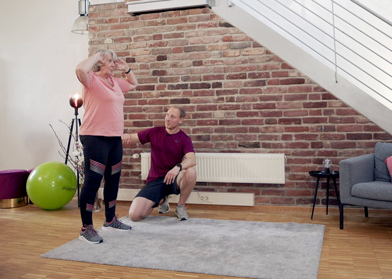 Trainer und ältere Frau beim Rückentraining mit Gymnastikball in Loftwohnung