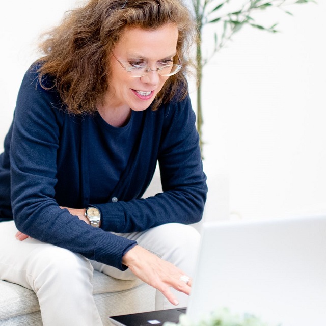 Frau mit Brille am Laptop sitzend und lächelnd