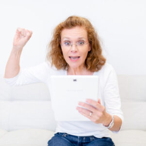Frau mit überraschtem Gesichtsausdruck hält Tablet und reckt Faust